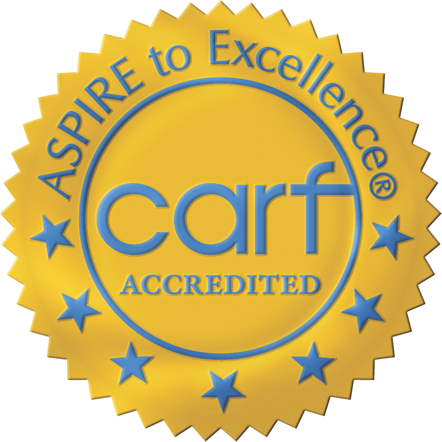 A gold seal with blue text reads, “ASPIRE to Excellence®” around the top edge and “carf ACCREDITED” in the center. Blue stars form a semi-circle at the bottom. The seal signifies CARF accreditation for Opioid Treatment Programs (OTPs).